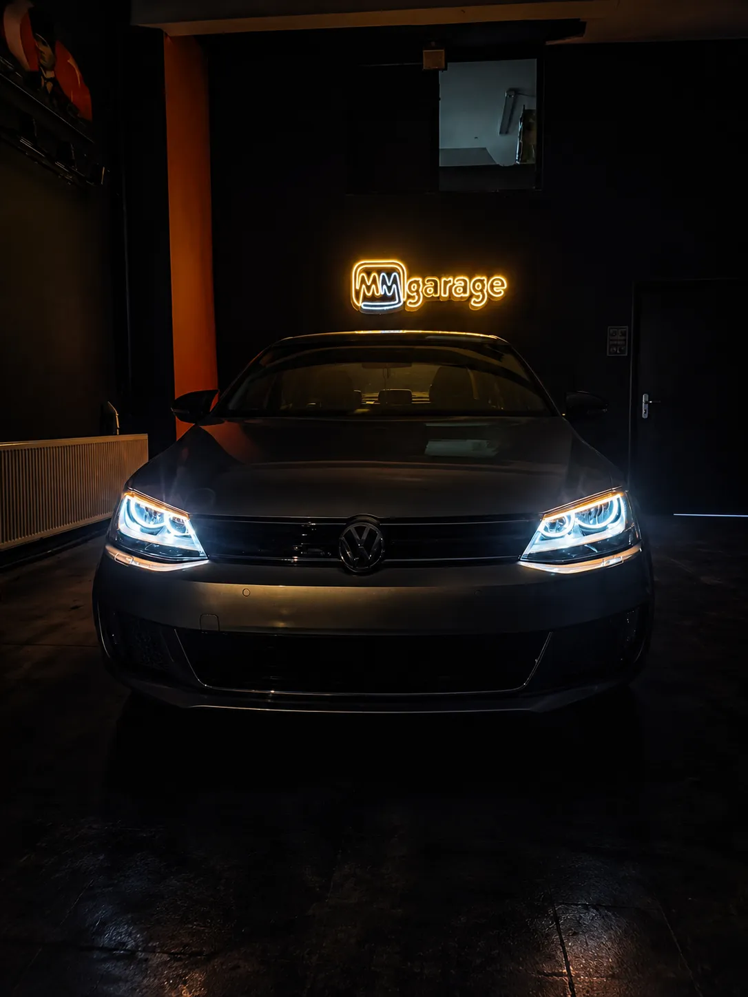 MM Garage atölyesinde ışıklı tabela önünde farları açık araç